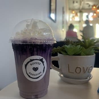 Iced ube latte with whipped cream in a Koffee Paradise cup